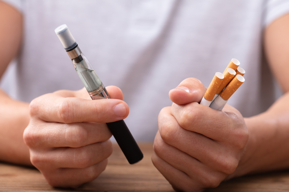 e-cigarette vs cigarette, homme tenant une e-cig et des cigarettes